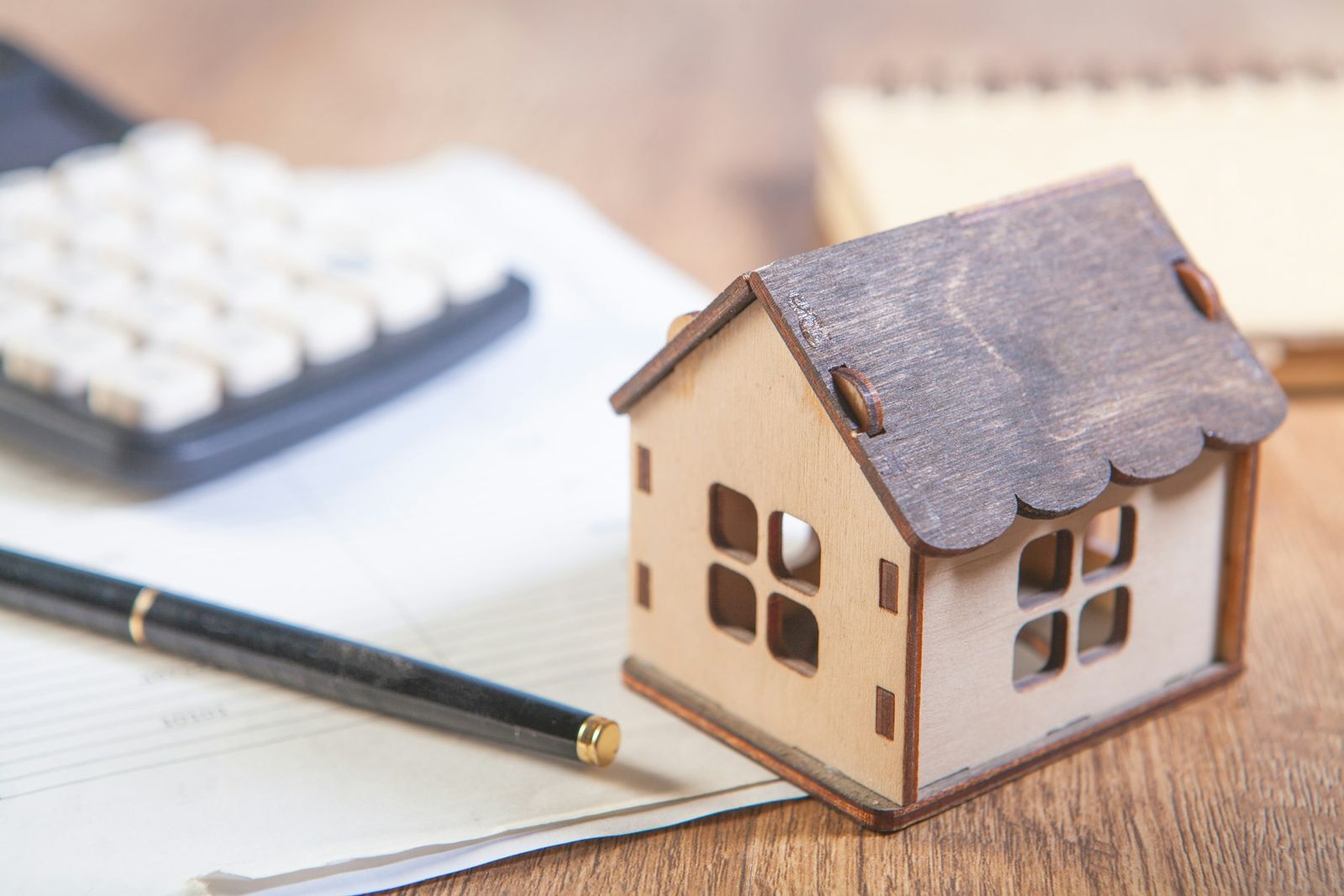 Ein Holzhaus-Modell mit Taschenrechner und Stift